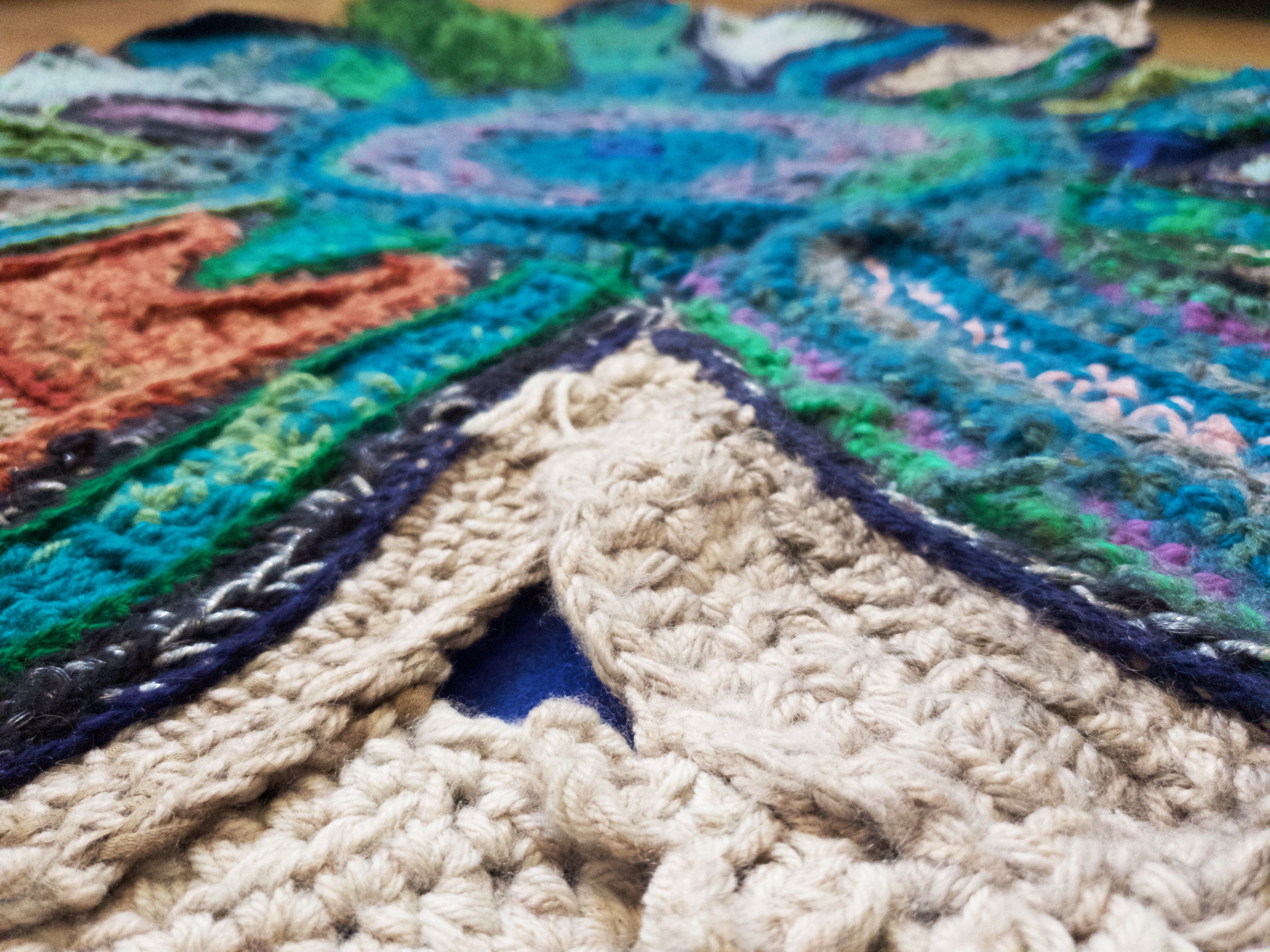 Close of of crochet rug sculpture in green, cream and orange