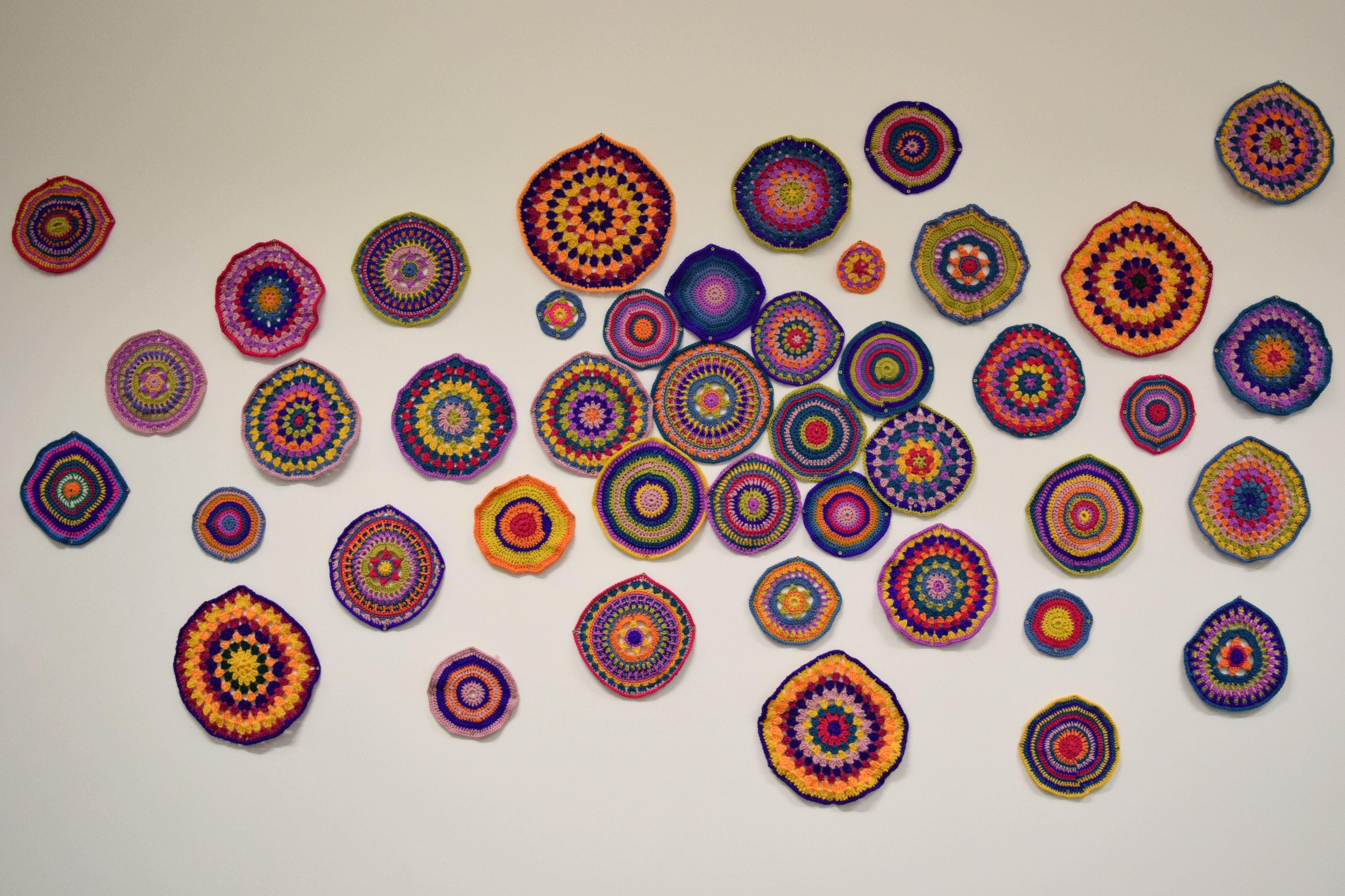 A multitude of brightly coloured crochet circles on a white wall