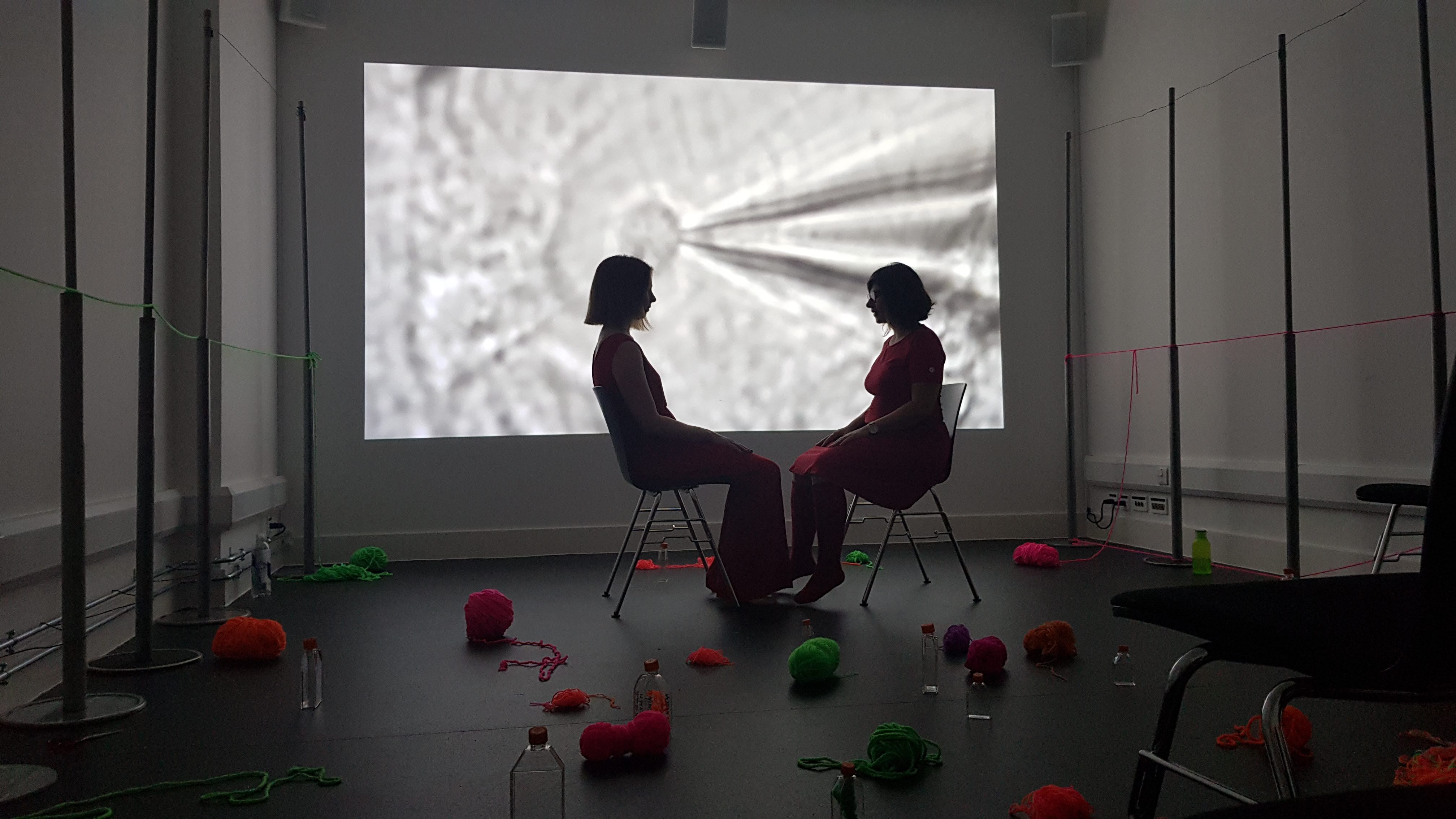 Artists Barbara Touati-Evans and Susan Merrick sitting opposite each other in front of neuroscience video