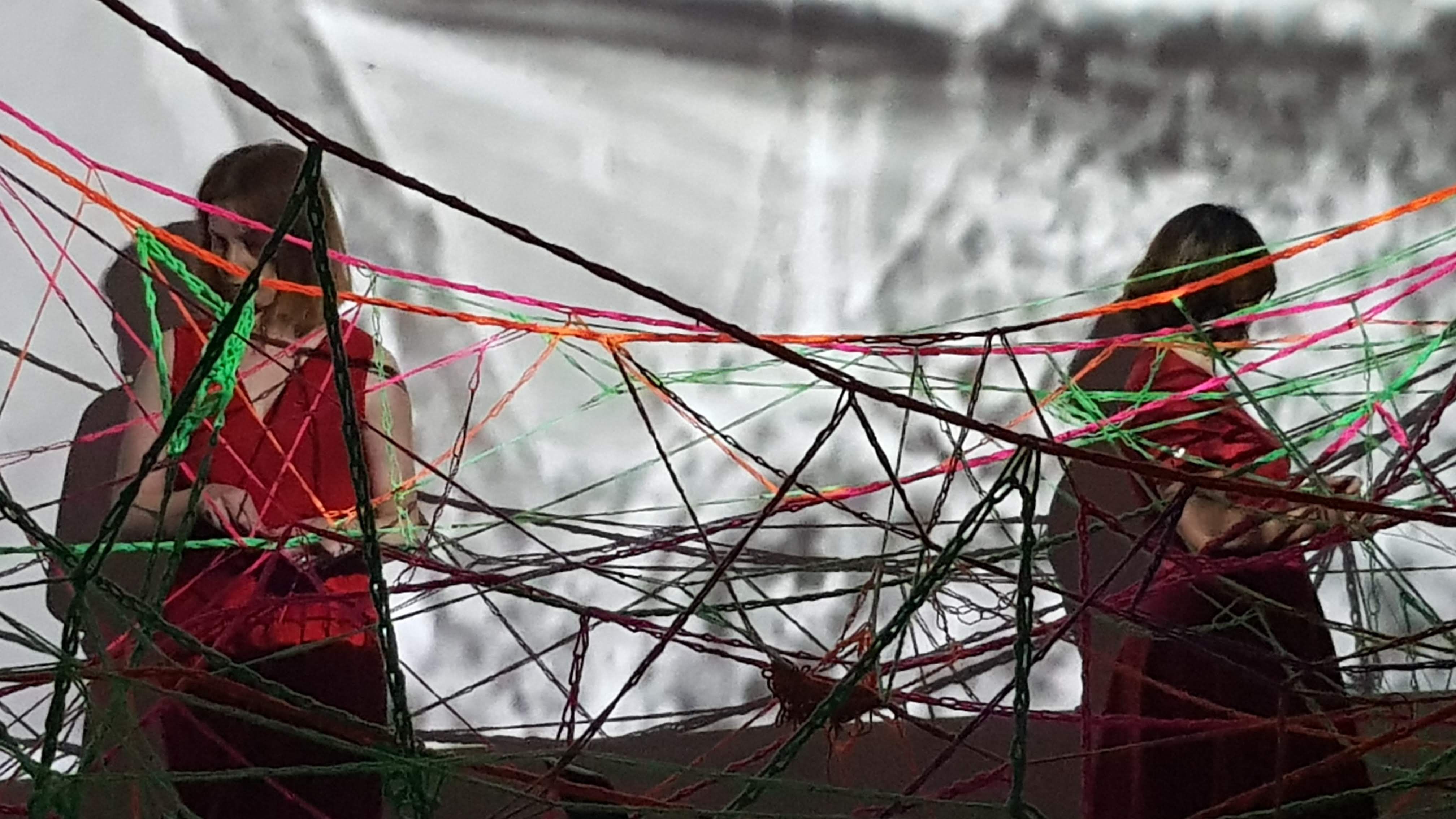 Artists Barbara Touati-Evans and Susan Merrick creating a wool web in front of a neuroscience video