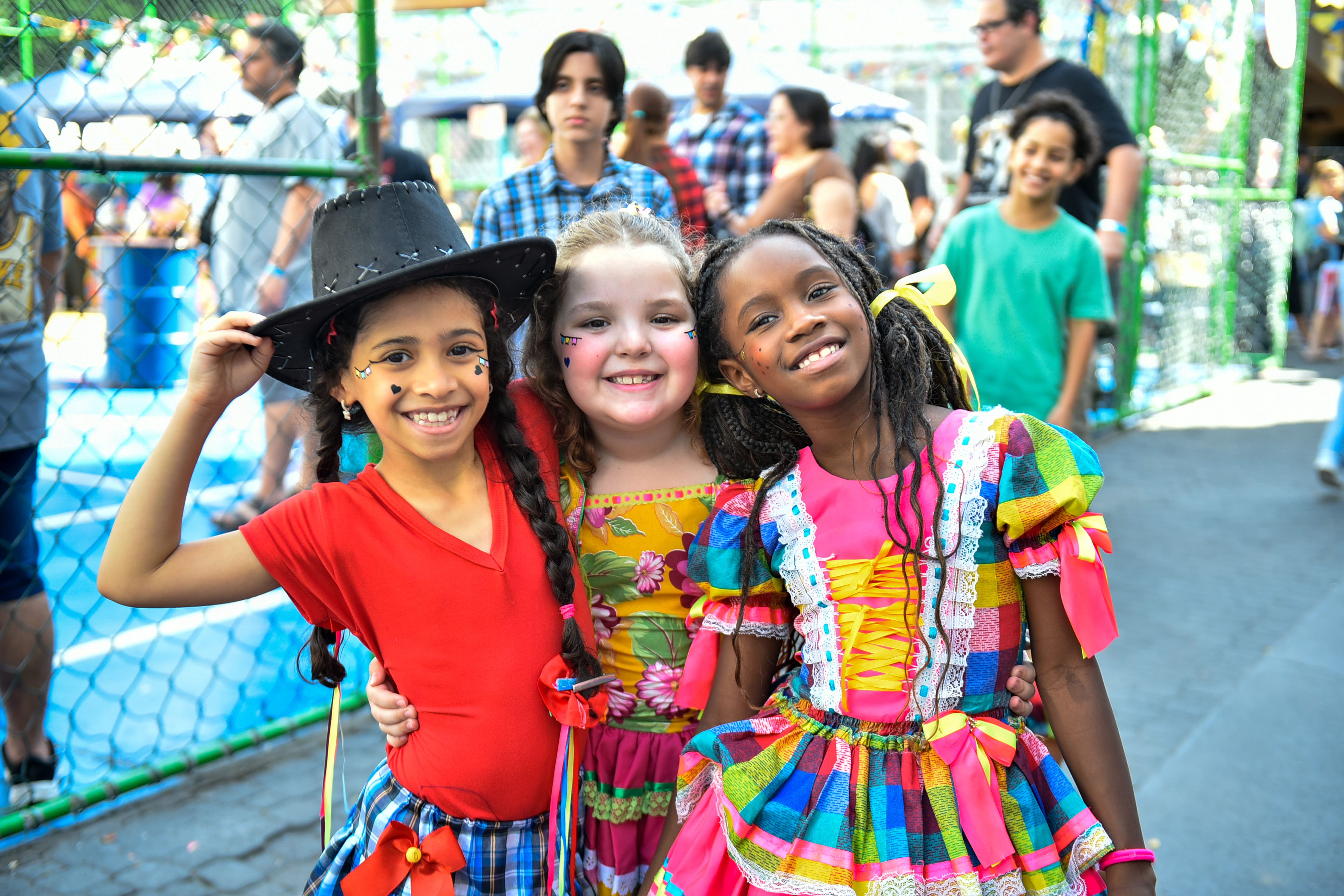 Três estudantes com trajes de festa junina posam juntas durante a celebração do Coração de Maria