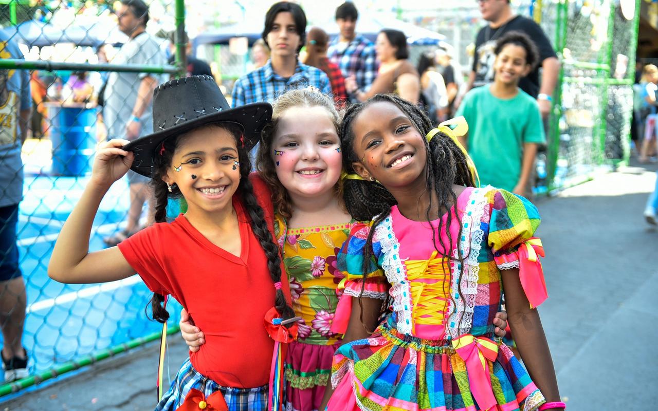 Três estudantes com trajes de festa junina posam juntas durante a celebração do Coração de Maria