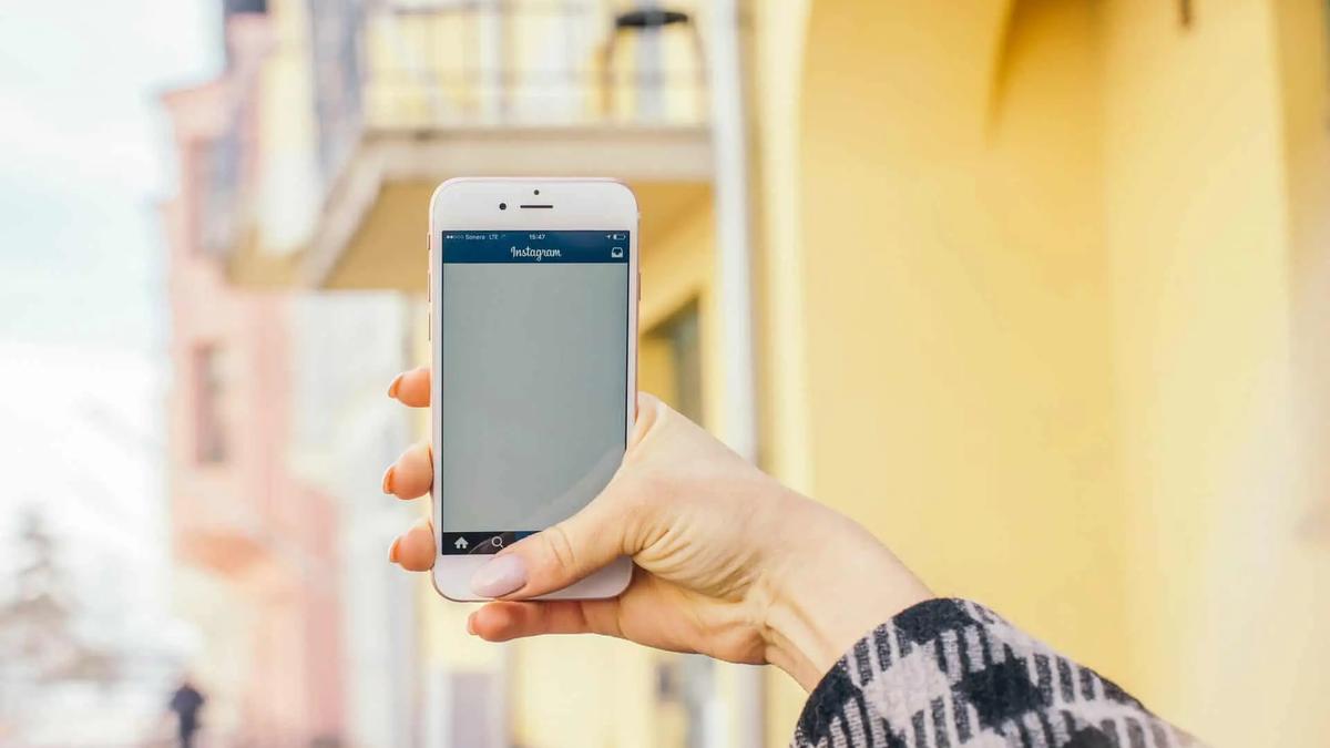 Una mano sostiene un telefono con la aplicacion de Instagram abierta, frente a un edificio amarillo