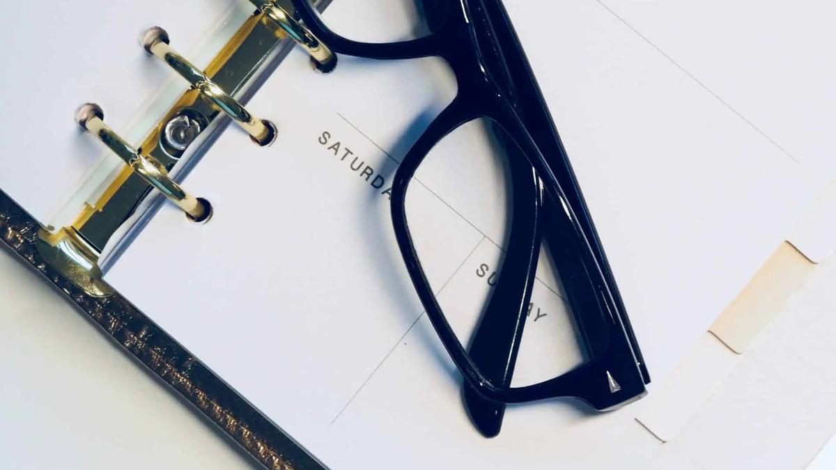 Black glasses resting on an open ring-bound planner showing days of the week