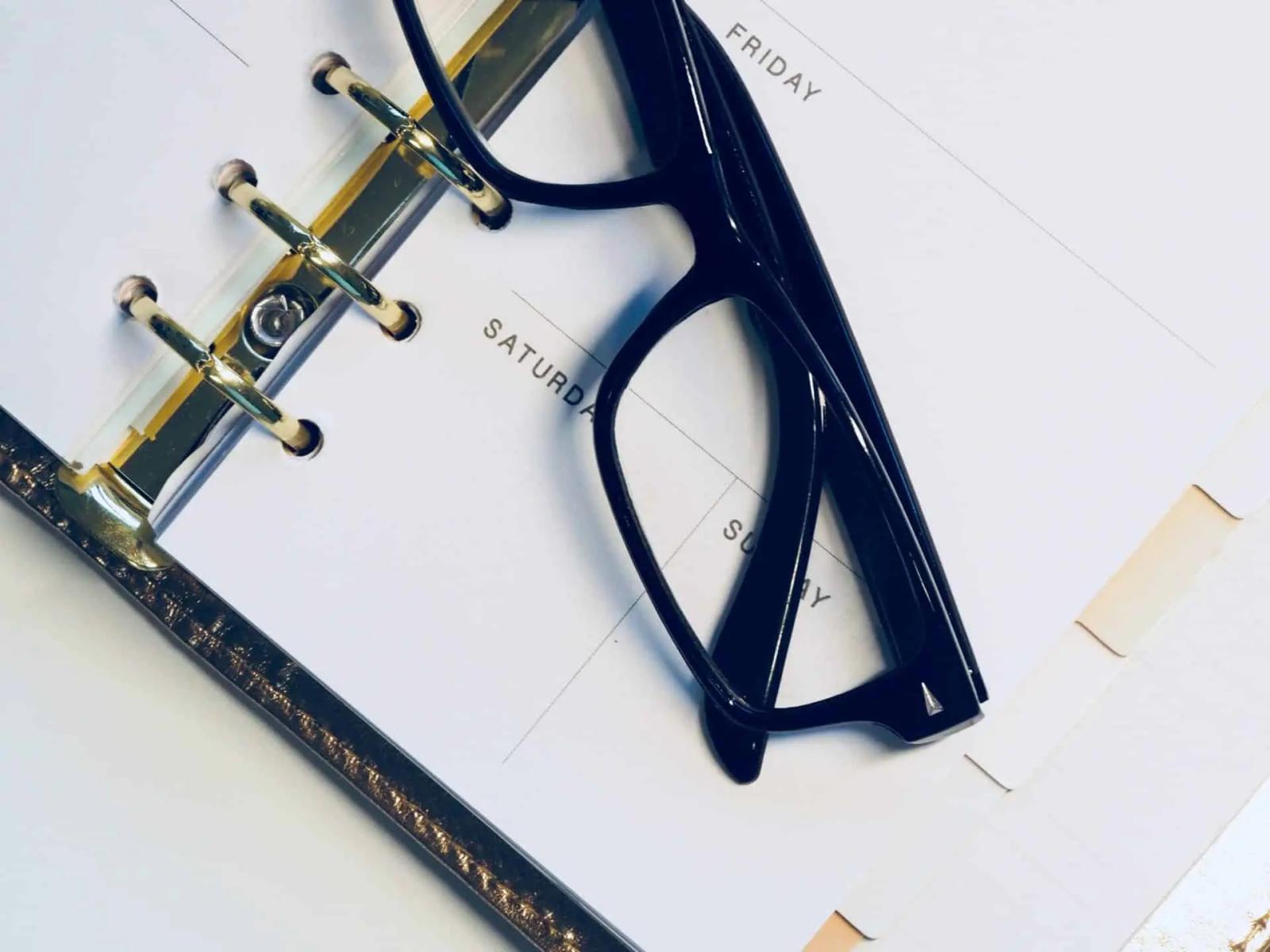 Unas gafas negras apoyadas sobre una agenda de anillas abierta con los días de la semana