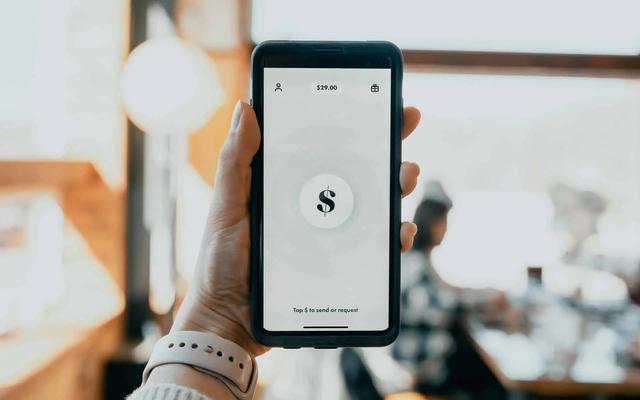 Mano sosteniendo un teléfono con una app de pago mostrando un símbolo de dólar