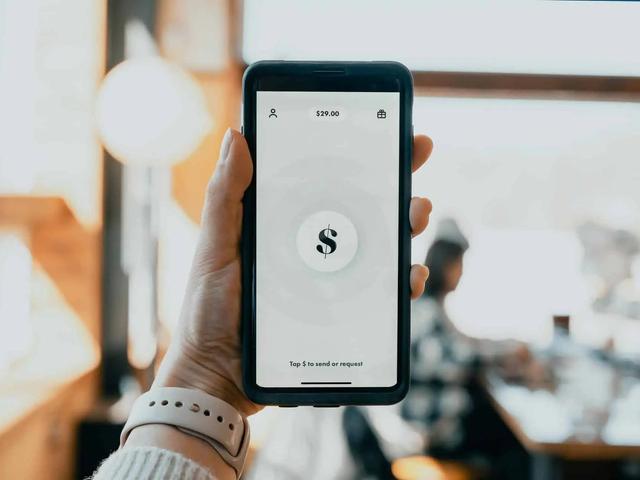 Mano sosteniendo un teléfono con una app de pago mostrando un símbolo de dólar