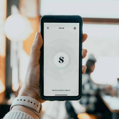 Mano sosteniendo un teléfono con una app de pago mostrando un símbolo de dólar