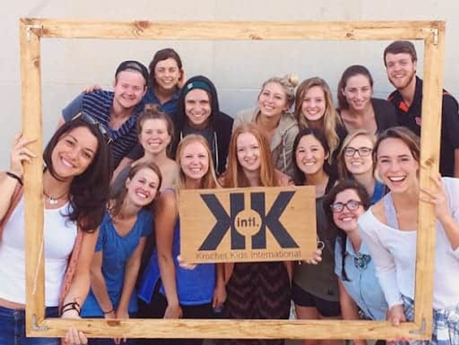 Un grupo de personas sonriendo juntas, sosteniendo un marco de madera y un cartel de Krochet Kids International.