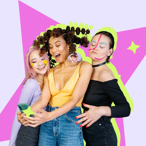 Three young women with colourful makeup taking a selfie together against a bright graphic backdrop.