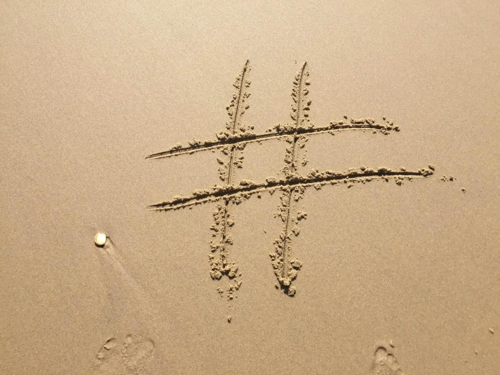 Un símbolo de hashtag dibujado en la arena, con huellas de pisadas cerca