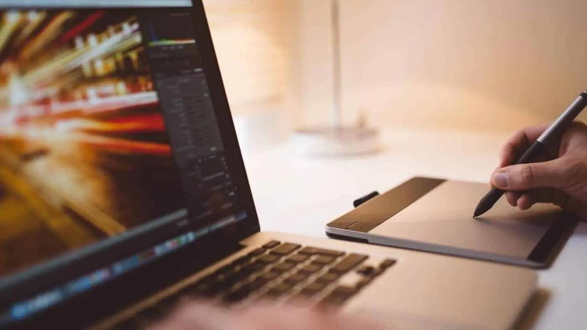 A person editing video footage on a laptop while using a stylus on a graphics tablet