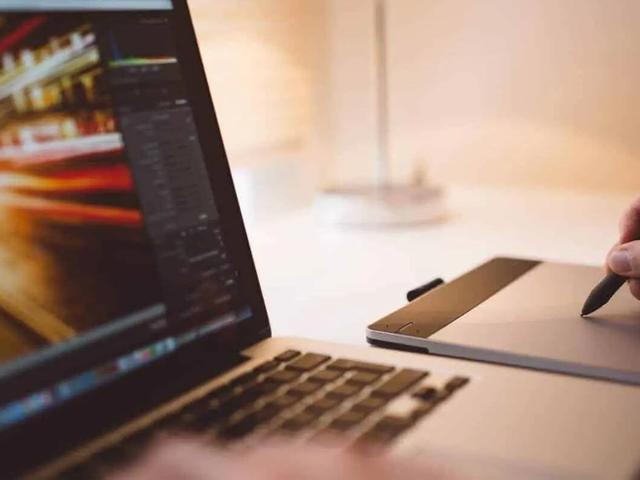 A person editing video footage on a laptop while using a stylus on a graphics tablet