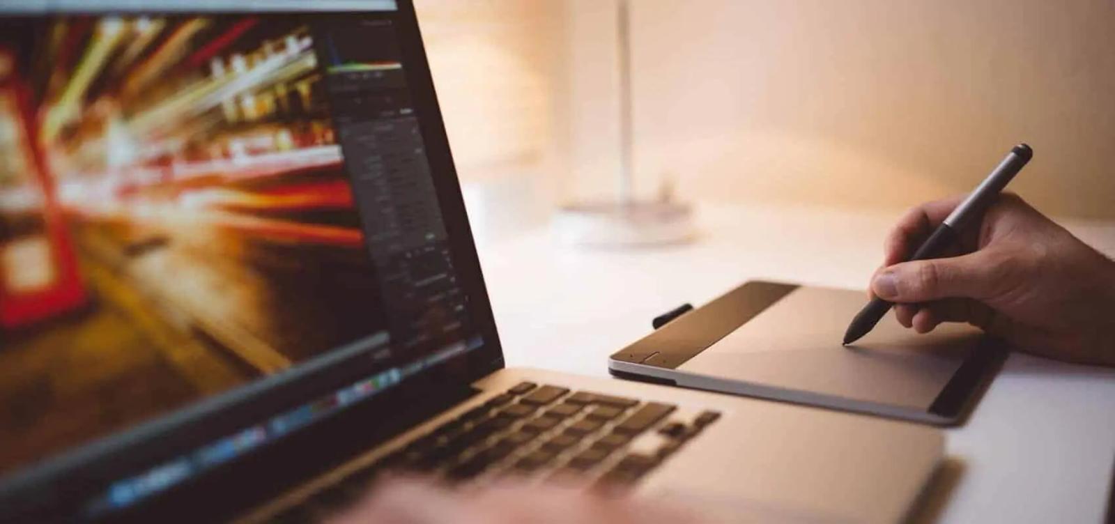 Una persona edita un video en una laptop mientras usa un lápiz óptico sobre una tableta gráfica