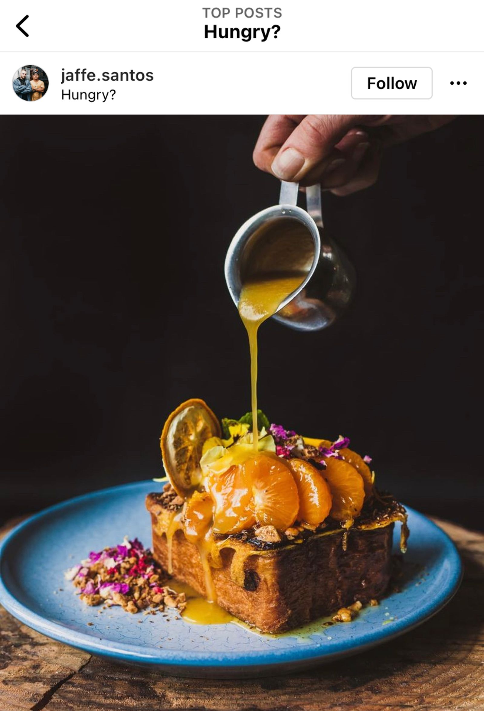 Instagram post of sauce being poured over a plated dessert topped with citrus and edible flowers