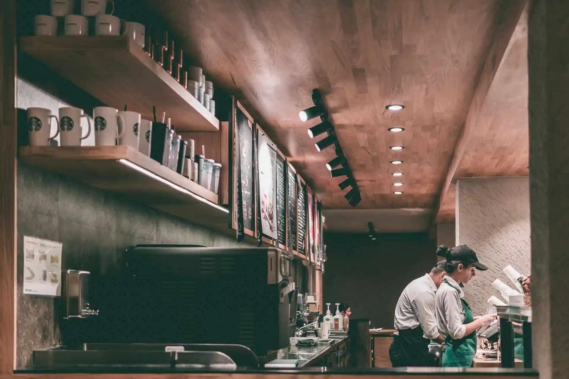 Baristas working behind the counter of a coffee shop with mugs and menu boards on shelves