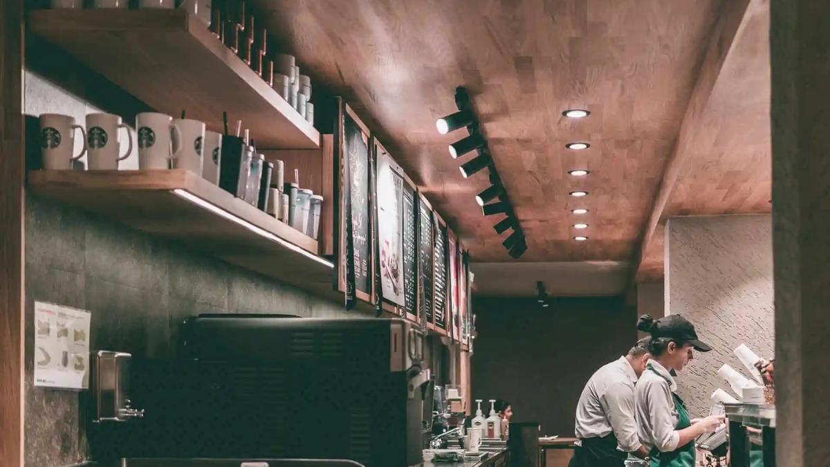 Baristas working behind the counter of a coffee shop with mugs and menu boards on shelves
