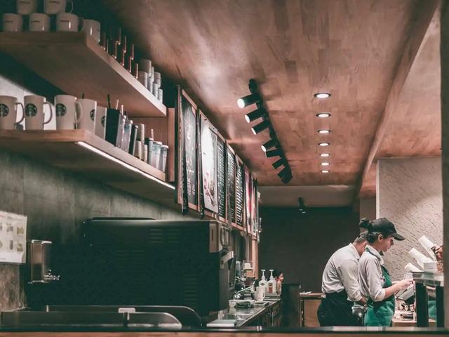 Baristas working behind the counter of a coffee shop with mugs and menu boards on shelves