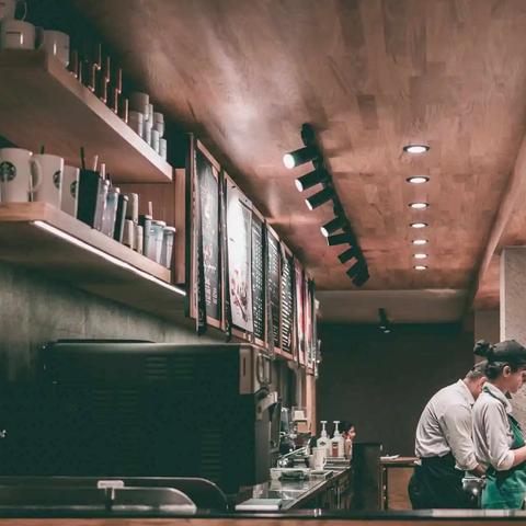 Baristas working behind the counter of a coffee shop with mugs and menu boards on shelves