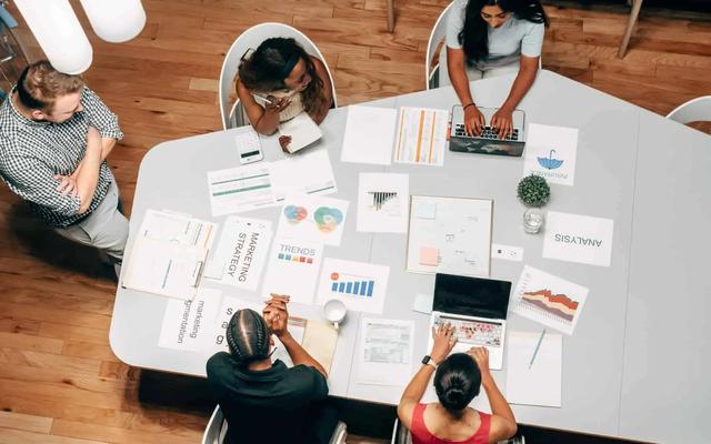 Vista aerea de un equipo reunido en una mesa con laptops, graficos y hojas de estrategia de marketing