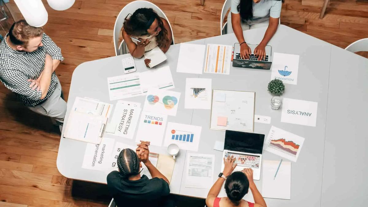 Overhead view of a team meeting around a table covered with charts, laptops and marketing strategy papers