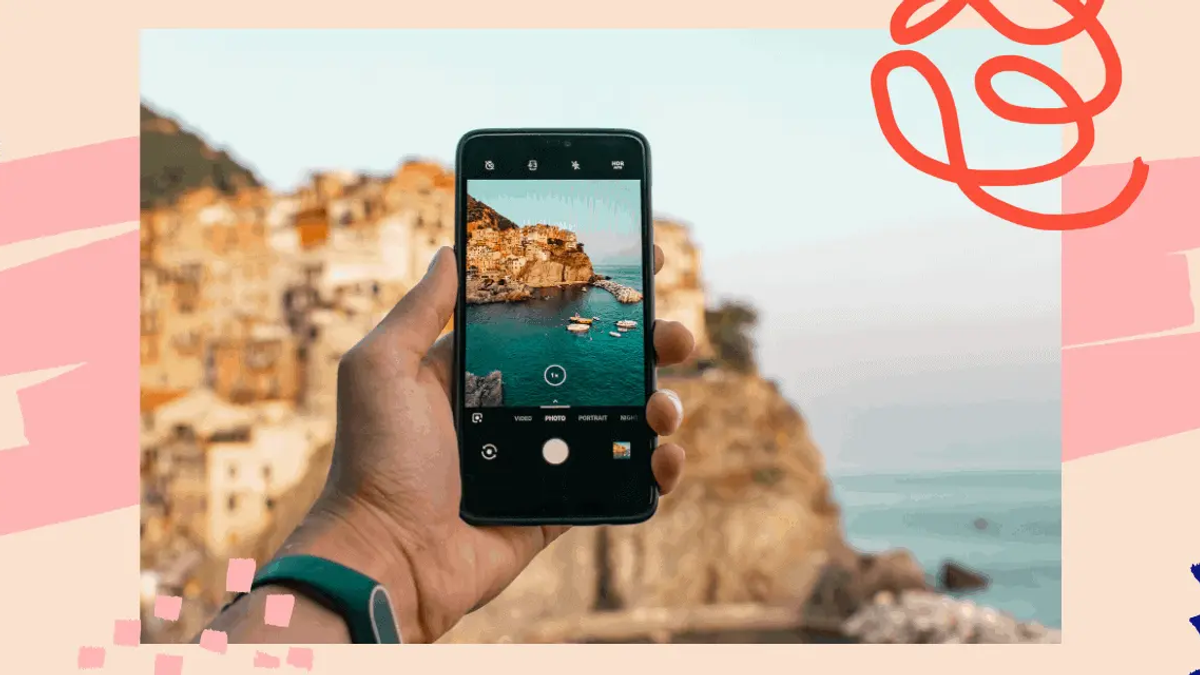 Hand holding a smartphone displaying a photo of a coastal town with boats in the water, against a colorful background.