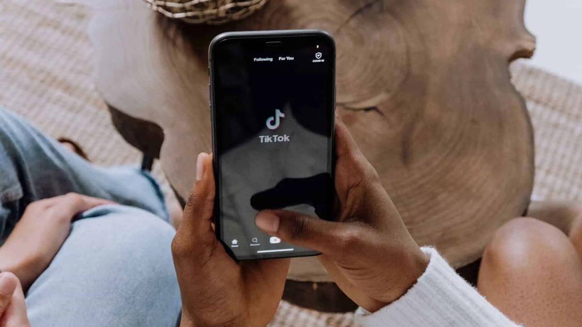 A person holds a phone displaying the TikTok app loading screen while seated indoors.