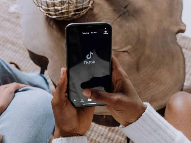 A person holds a phone displaying the TikTok app loading screen while seated indoors.