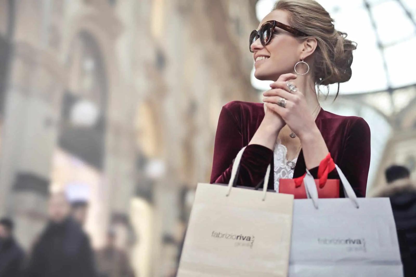 Mujer sonriente con gafas de sol sosteniendo bolsas de compras en una calle de la ciudad