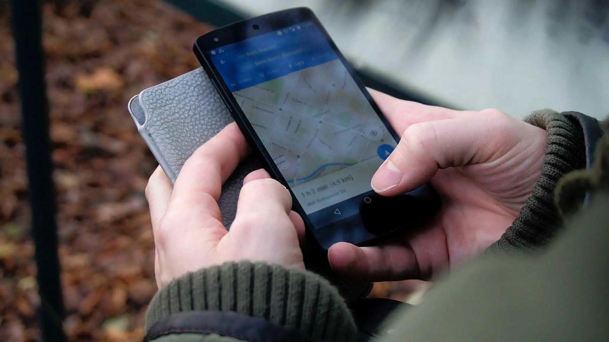 Hands holding a smartphone displaying a map application with a route and travel time of 1h 2 min (4.9 km)