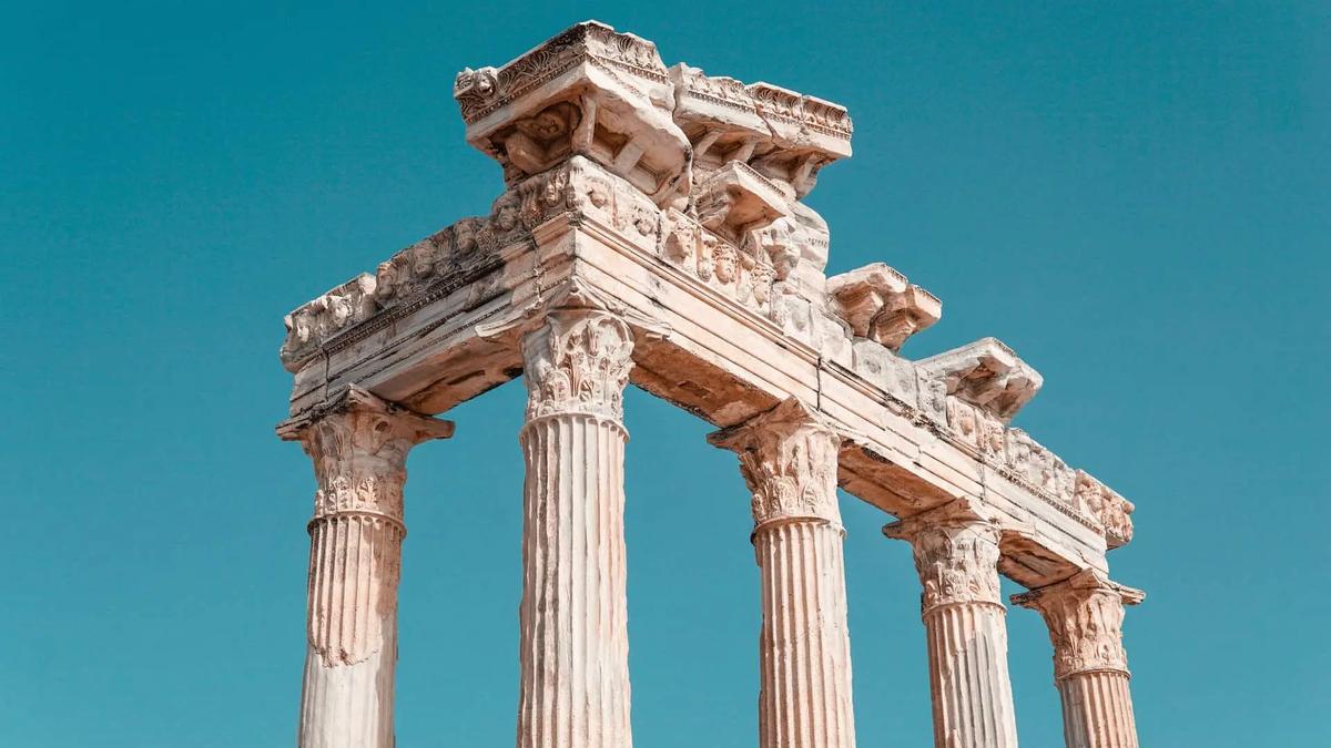 Ruinas de antiguas columnas de piedra que sostienen un entablamento tallado bajo un cielo azul
