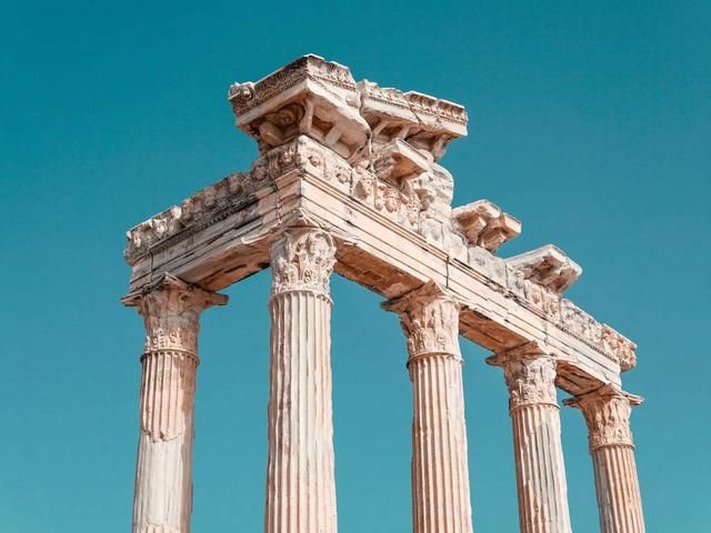 Ruinas de antiguas columnas de piedra que sostienen un entablamento tallado bajo un cielo azul