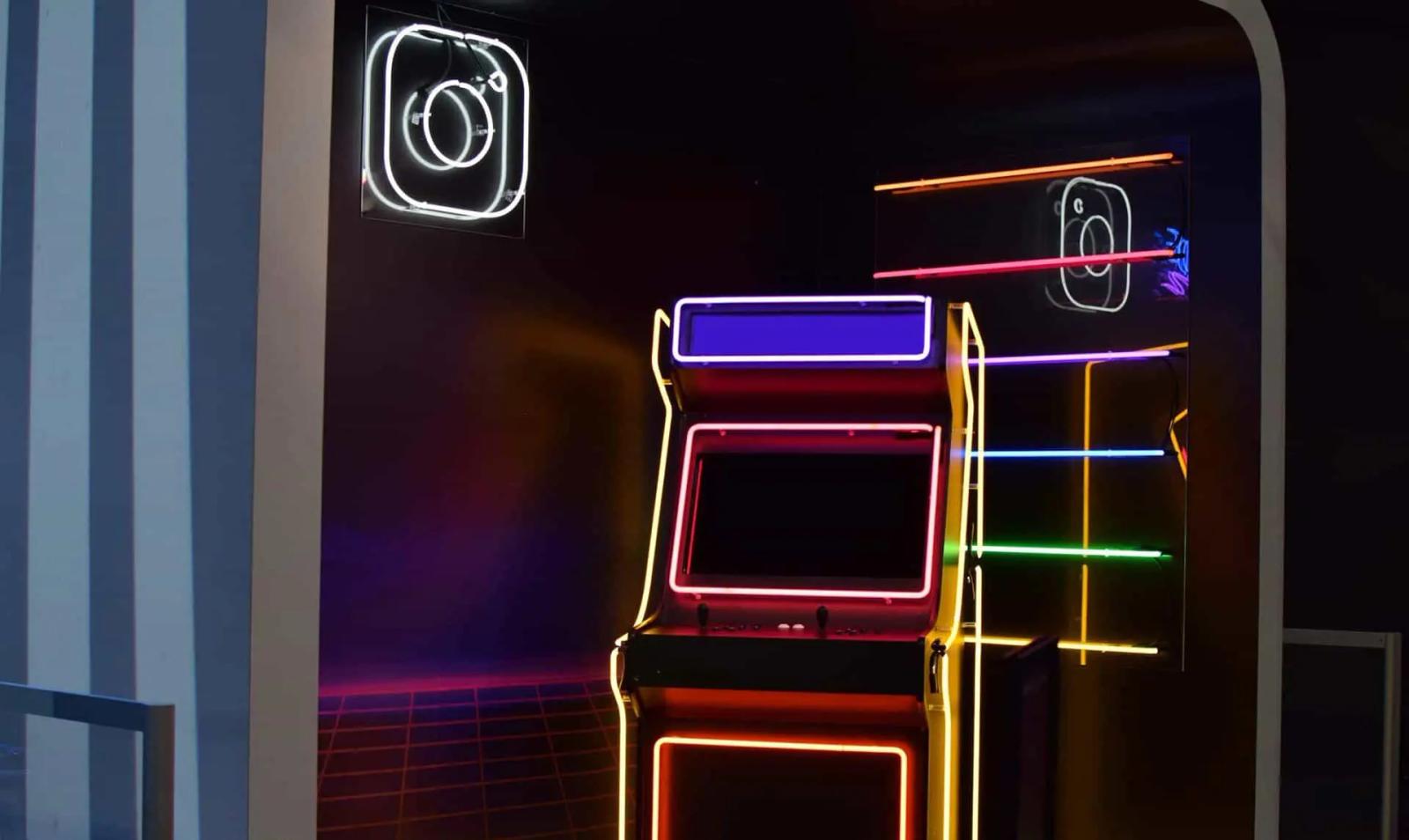 Una máquina arcade con luces de neón junto a un letrero luminoso del logo de Instagram