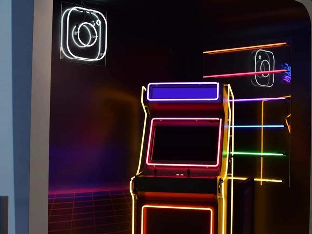 Una máquina arcade con luces de neón junto a un letrero luminoso del logo de Instagram