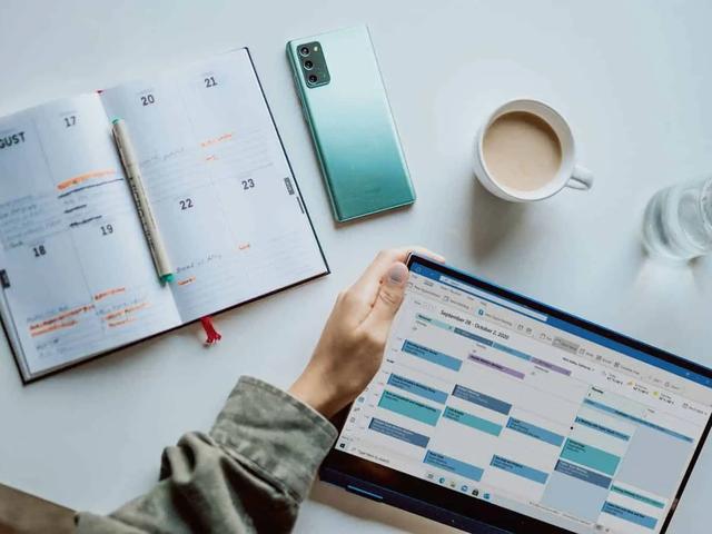 Una agenda de papel, un teléfono, un café y un portátil con un calendario semanal en la pantalla