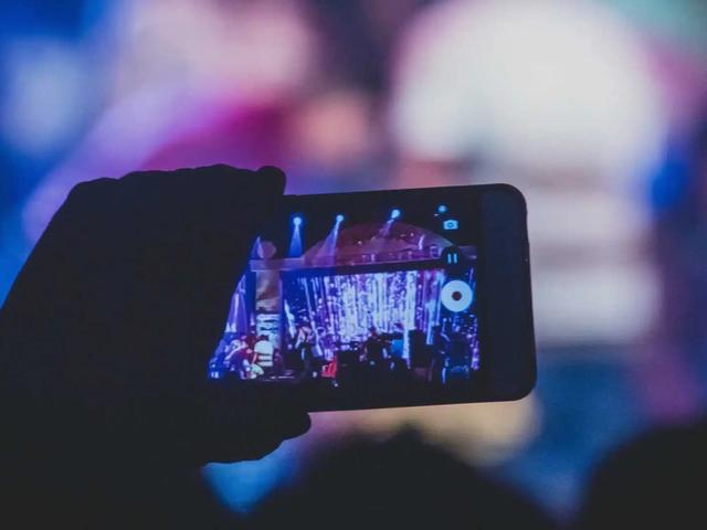 A hand holds up a phone recording video of a concert stage in a dark venue