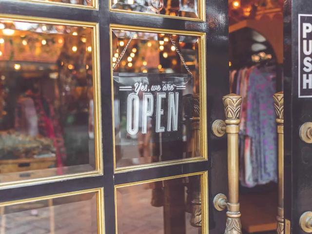 A glass shop door with an open sign, gold handles, and clothing racks visible inside