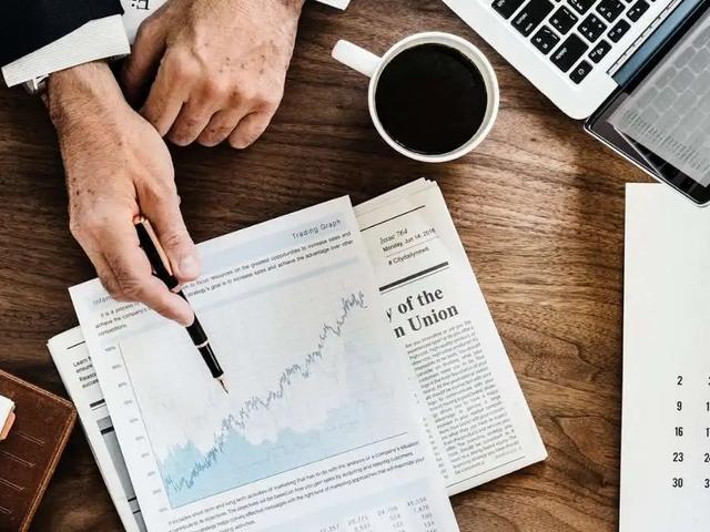 Manos señalando un gráfico impreso sobre un escritorio con periódico, café y un calendario