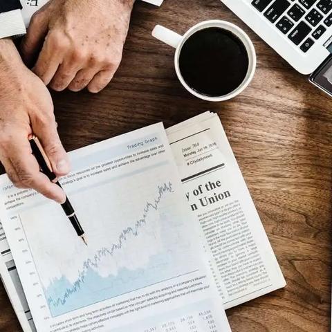 Manos señalando un gráfico impreso sobre un escritorio con periódico, café y un calendario