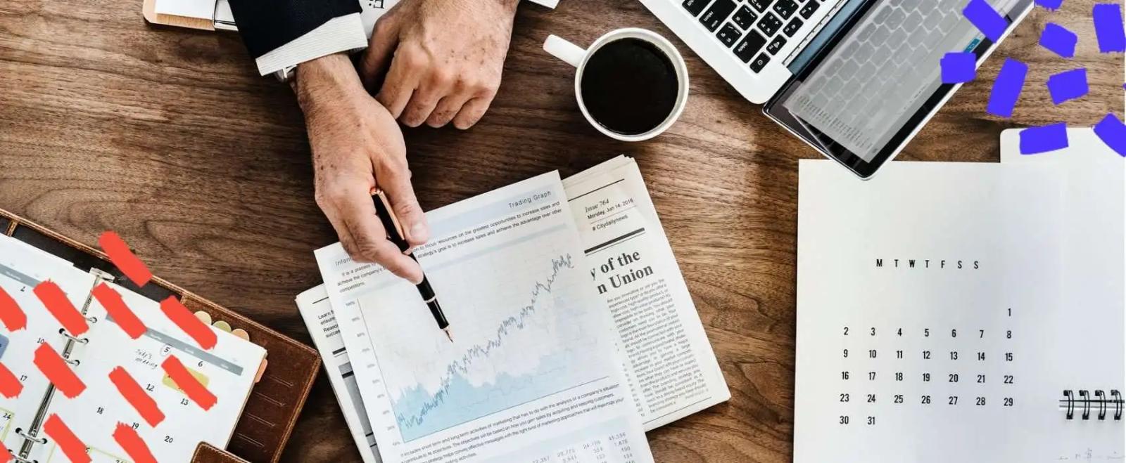 Manos señalando un gráfico impreso sobre un escritorio con periódico, café y un calendario