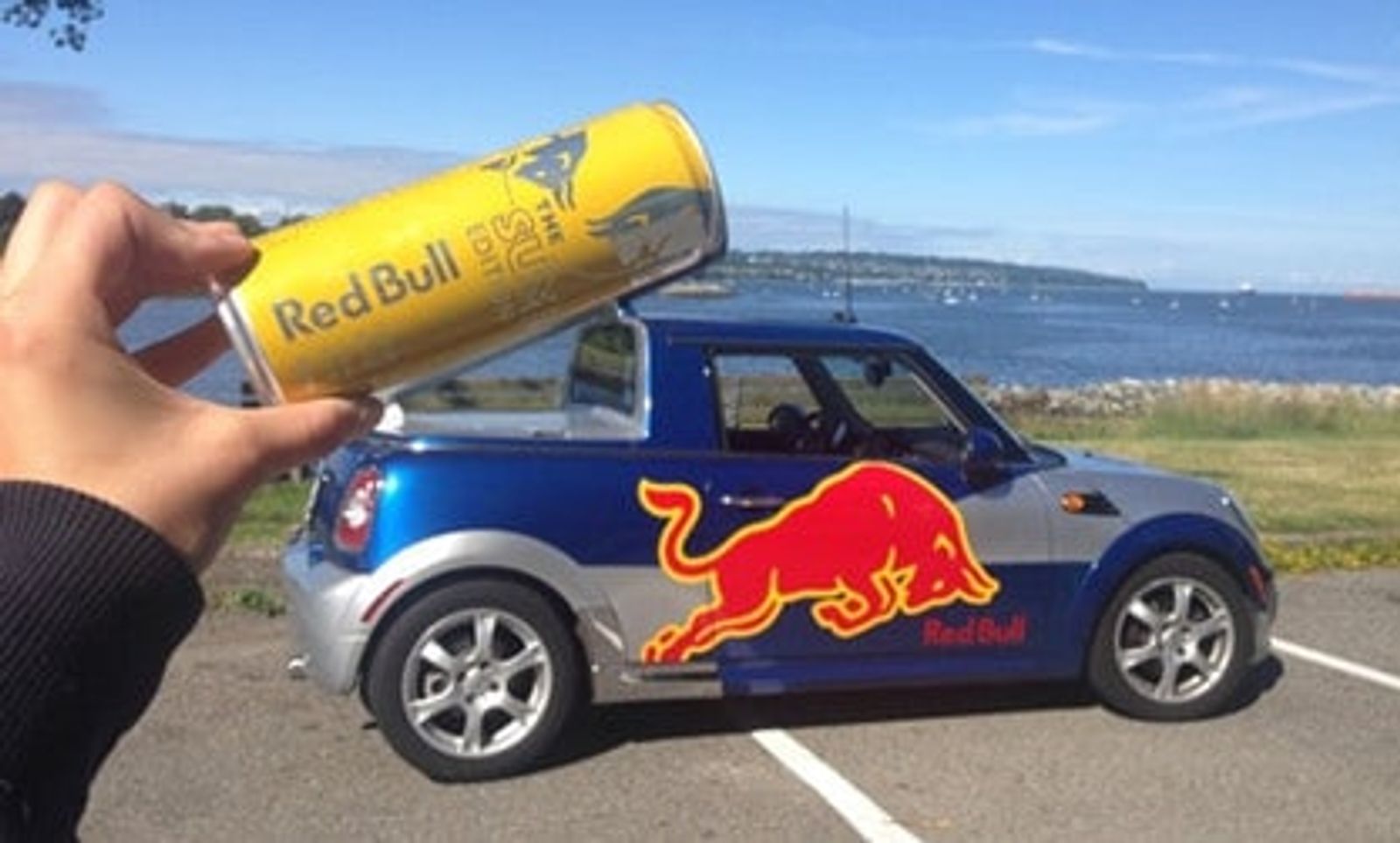 Persona sosteniendo una lata de Redbull sobre un carro Mini de Redbull