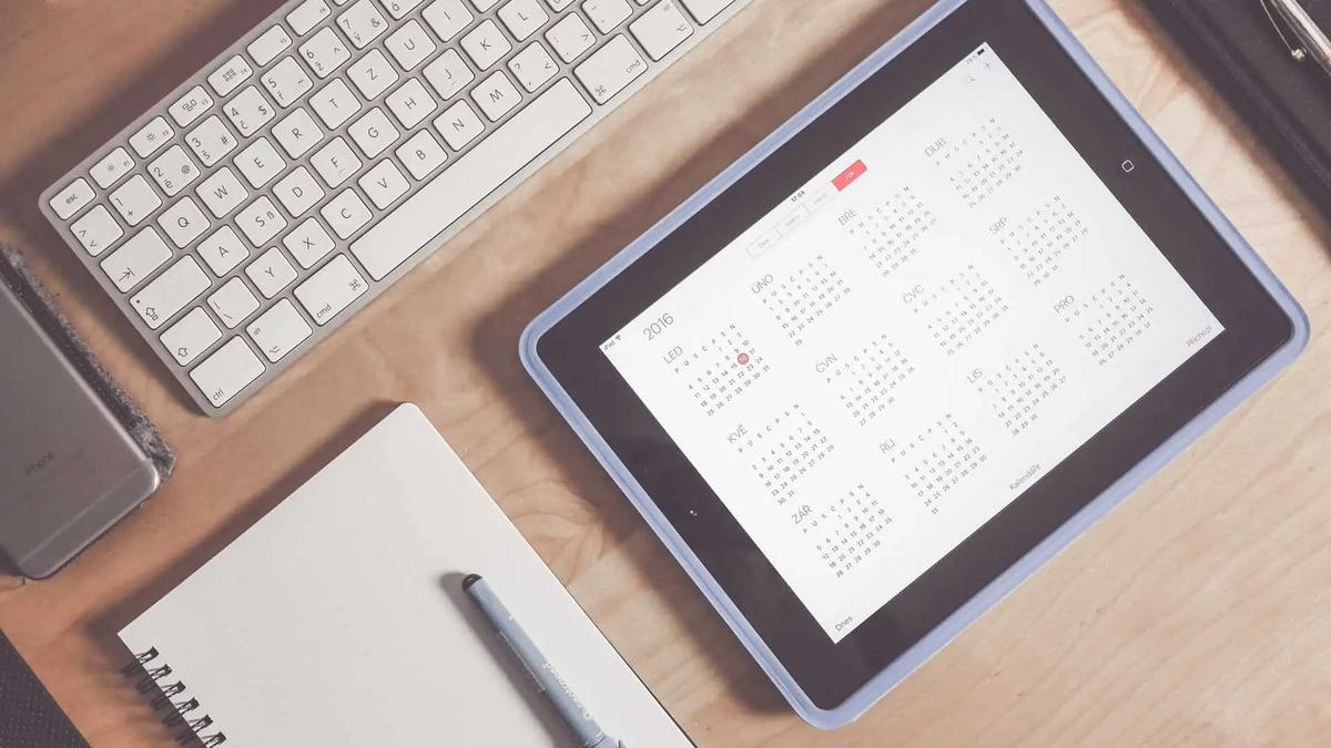 Overhead view of a desk with a keyboard, notebook, phone and a tablet showing a yearly calendar app