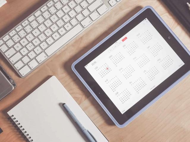 Vista cenital de un escritorio con teclado, cuaderno, teléfono y una tableta con una app de calendario anual