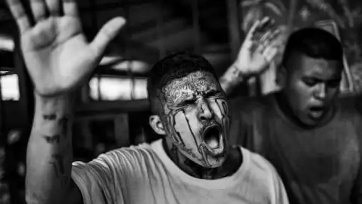 Hombre con tatuajes faciales y brazos alzados, gritando en un momento de intensa emoción, foto en blanco y negro