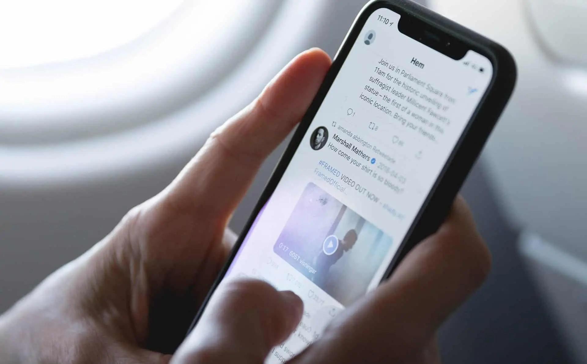 Una mano desplaza el feed de una red social en un smartphone junto a la ventanilla de un avion