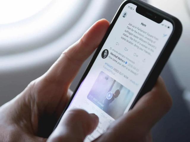A hand scrolling a social media feed on a smartphone near an airplane window