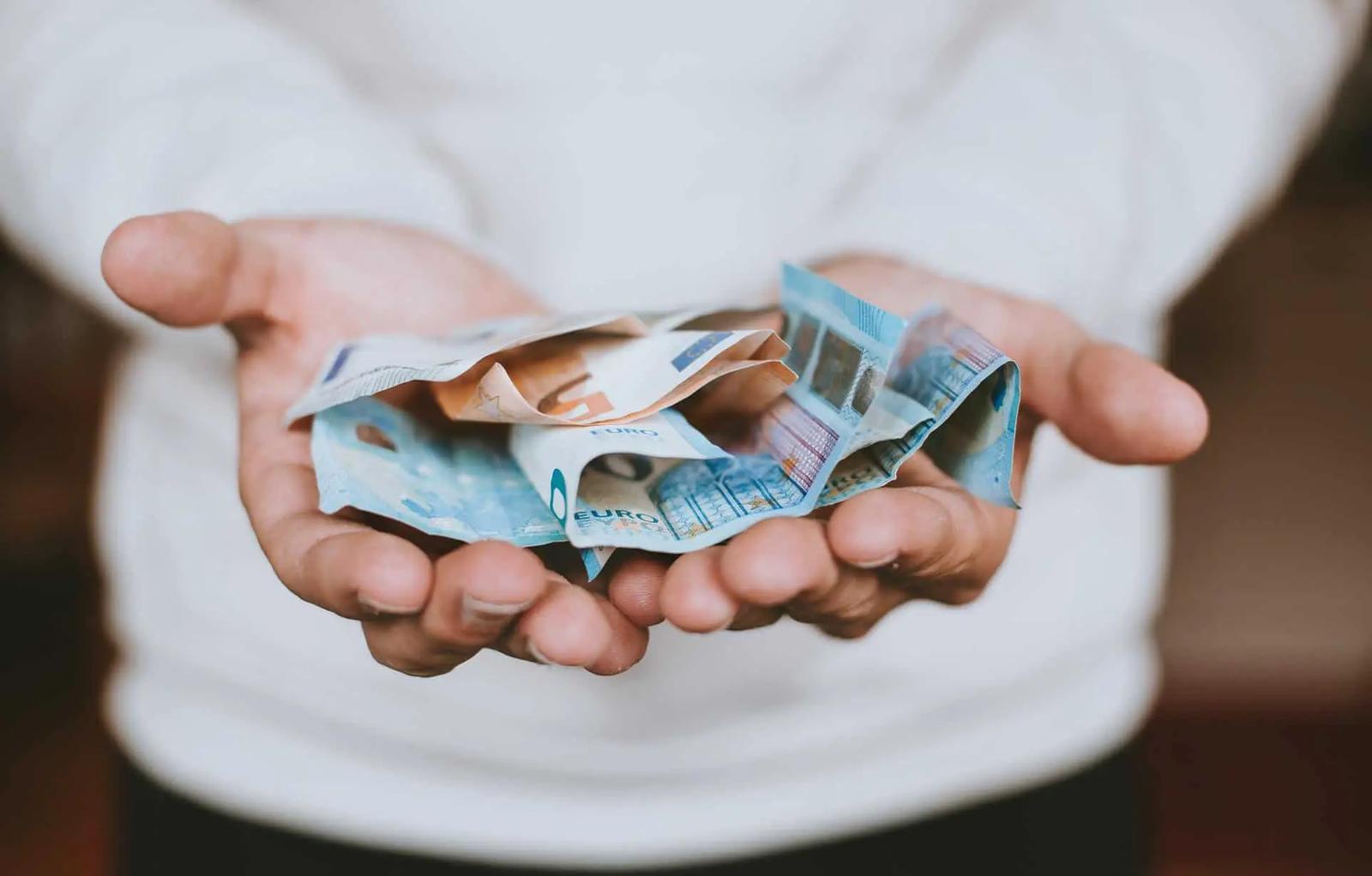 Cupped hands holding a crumpled fan of euro banknotes