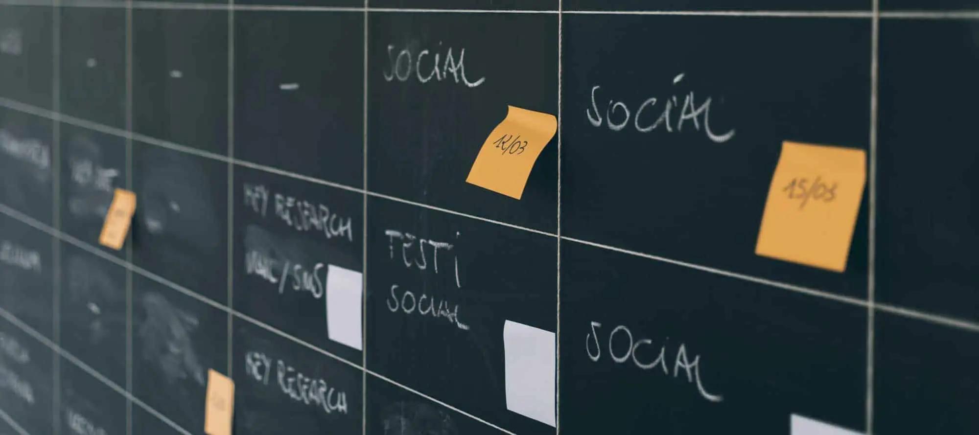 Una pizarra con una cuadrícula de planificación, etiquetas en tiza como Social y notas adhesivas naranjas con fechas
