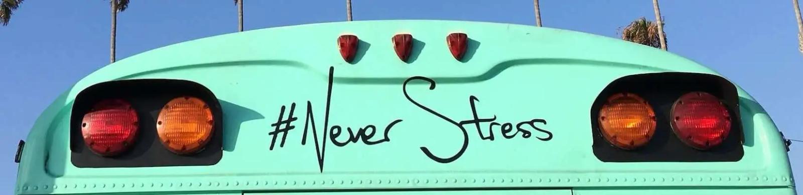 Back of a mint green bus with taillights and a hand painted hashtag never stress under palm trees