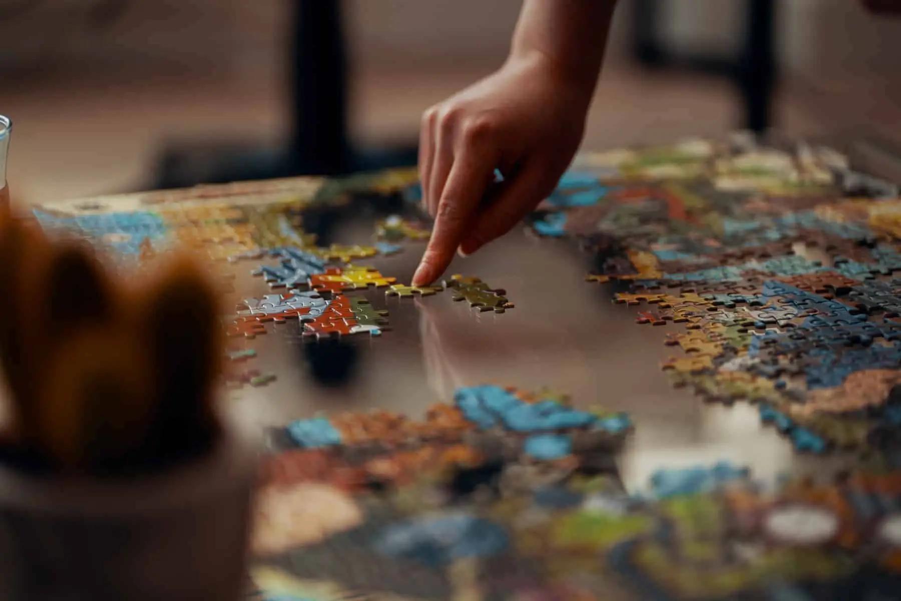 A hand placing a piece into a partly finished jigsaw puzzle on a table